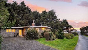 A single-story house with a stone facade, a visible chimney, and a gravel driveway. - Four Bears by Avantstay Walk to Beach, Hot Tub, Ocean View (Arch Cape)