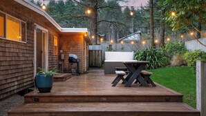 A wooden deck with a barbecue and hot tub, surrounded by a wooden fence and trees. - Four Bears by Avantstay Walk to Beach, Hot Tub, Ocean View (Arch Cape)