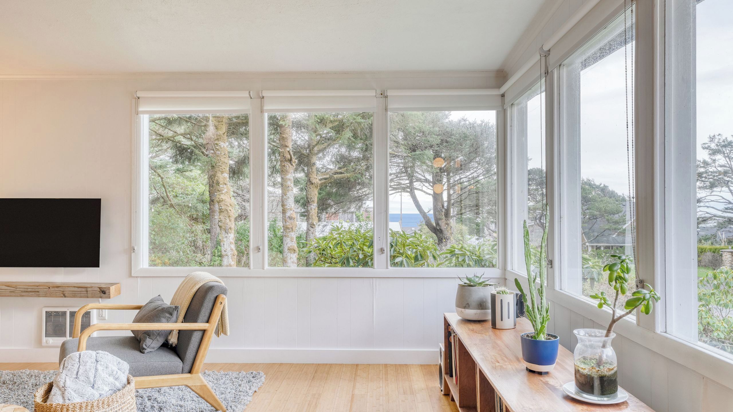 Ein Zimmer mit großem Fenster, Fernseher, Stuhl, kleinem Tisch mit Pflanzen und Holzboden.