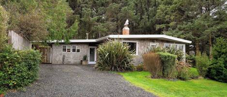 A single-story house with a gravel driveway, surrounded by dense forest.