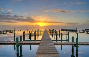 A wooden pier extending into calm water with a sunset in the background.