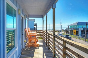 A wooden deck with a table and chairs, overlooking a beach and a road with cars.