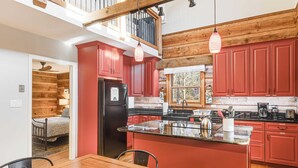 Una cocina moderna con armarios rojos, un refrigerador negro y una mesa de comedor de madera.