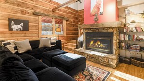 Un acogedor interior de cabaña de madera con chimenea de piedra, un sofá de cuero negro y una estantería.