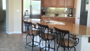 A modern kitchen with wooden cabinets, a stainless steel refrigerator, a coffee maker, and a sink. - Cassius model house and casita for rent in December 2025 (La Quinta)