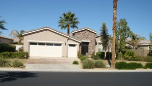 A residential house with a garage, a stone facade, and a well-maintained front yard with various plants. - Cassius model house and casita for rent in December 2025 (La Quinta)