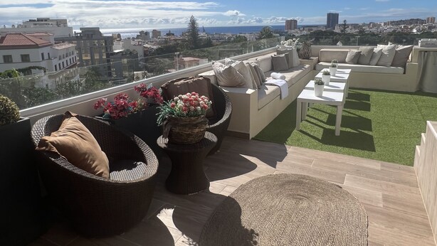 Una terraza en la azotea con mobiliario de mimbre, un sofá y una mesa.