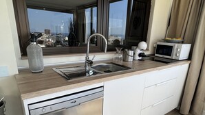 Una cocina moderna con un lavamanos de acero inoxidable, lavavajillas, microondas y ventana con vista a la ciudad.