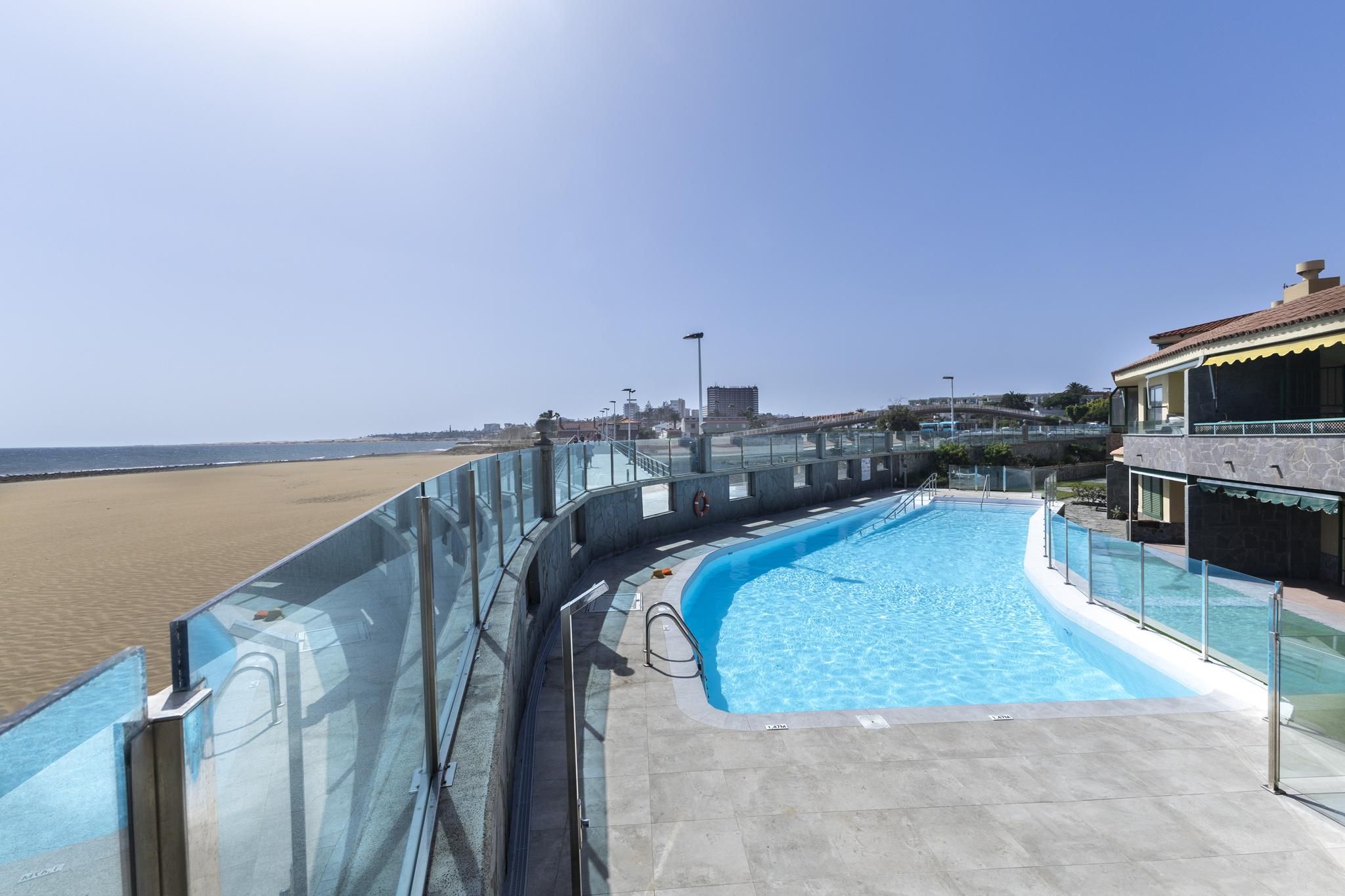Ein Schwimmbecken mit Glasbarriere, Blick auf den Strand und ein Gebäude mit Balkon.