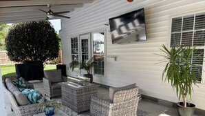En overdækket terrasse med fletmøbler, et fladskærms-TV på væggen og en potteplante.