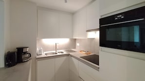 Una cocina compacta con armarios blancos, un horno negro, una cafetera y un tostador.