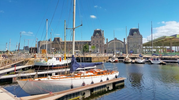 Un puerto deportivo con barcos amarrados, un edificio grande con una torre de reloj y un área cubierta con bicicletas.