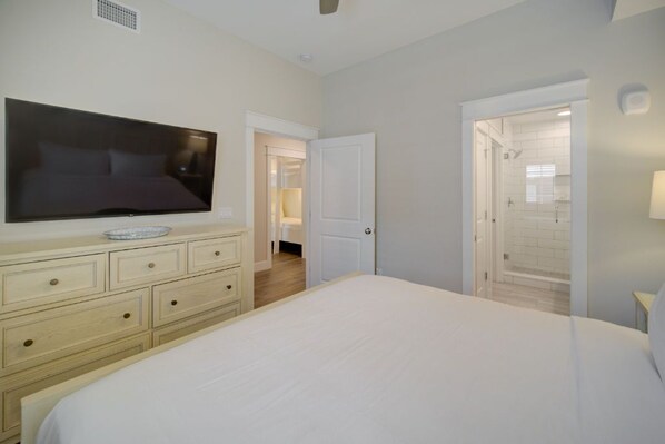 A bedroom with a large bed, a dresser, a flat-screen TV, and a walk-in closet.