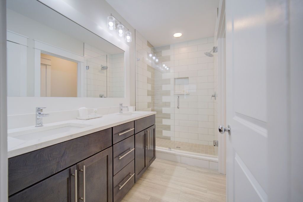 Une salle de bain moderne avec un grand miroir, deux lavabos, des meubles sombres et un espace douche.