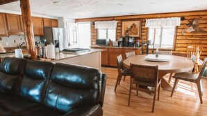 Un acogedor interior de cabaña con una mesa de comedor de madera, un sofá de cuero y una cocina equipada con electrodomésticos modernos.