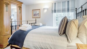 Un lit bien fait, recouvert d’une couvre-lit à rayures, une armoire en bois, un tableau encadré accroché au mur et une fenêtre agrémentée d’une lambrequin à rayures.