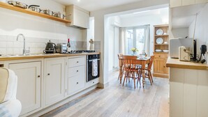 Une cuisine moderne avec des meubles en bois, un coin repas avec une table et des chaises en bois, et une vue sur l’extérieur par une fenêtre.