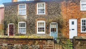 Une maison traditionnelle en briques, dont les murs sont recouverts de lierre, avec de nombreuses fenêtres et un mur en pierre à l’avant.