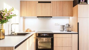 Une cuisine moderne avec des meubles en bois, un four encastré, une machine à café et un vase rempli de fleurs posé sur le plan de travail.