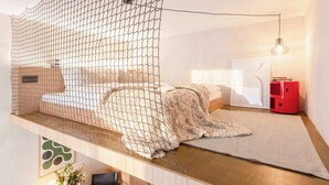 Une pièce comprenant un lit, une armoire rouge, un luminaire suspendu et une étagère fixée au mur.