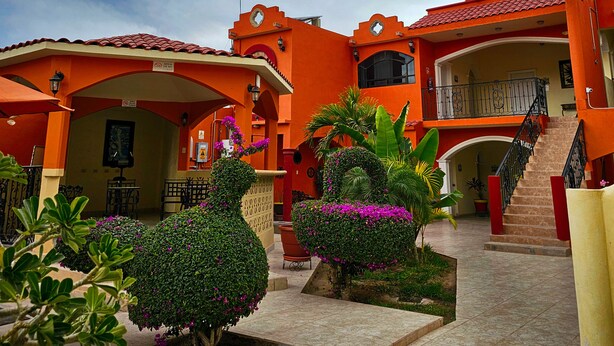 A courtyard with a staircase leading to a balcony, surrounded by orange buildings and lush greenery. - Hotel Oasis (Comondu)