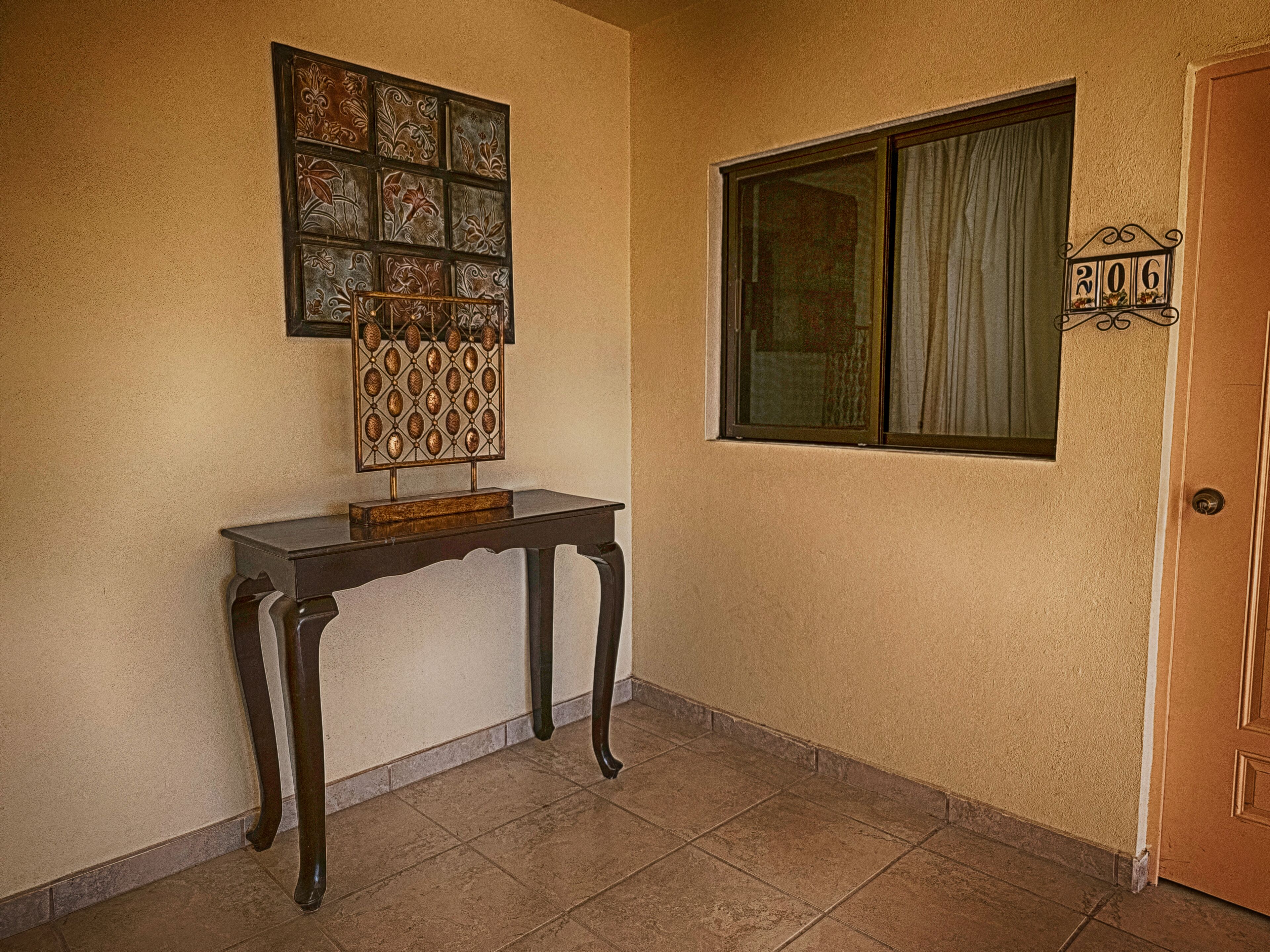 A hallway with a decorative wall piece, a door with a number plaque, and a window with curtains.
