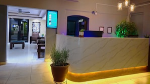 A hotel reception area with a marble counter, potted plants, and a digital display listing room types and prices. - Hotel Oasis (Comondu)