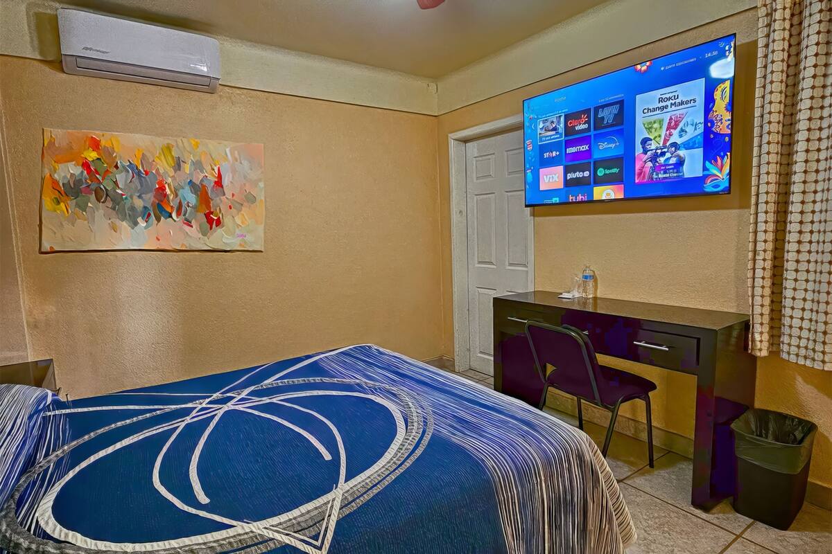Hotelkamer met een bed, bureau, stoel, tv aan de muur met een streamingdienst interface, en een schilderij.