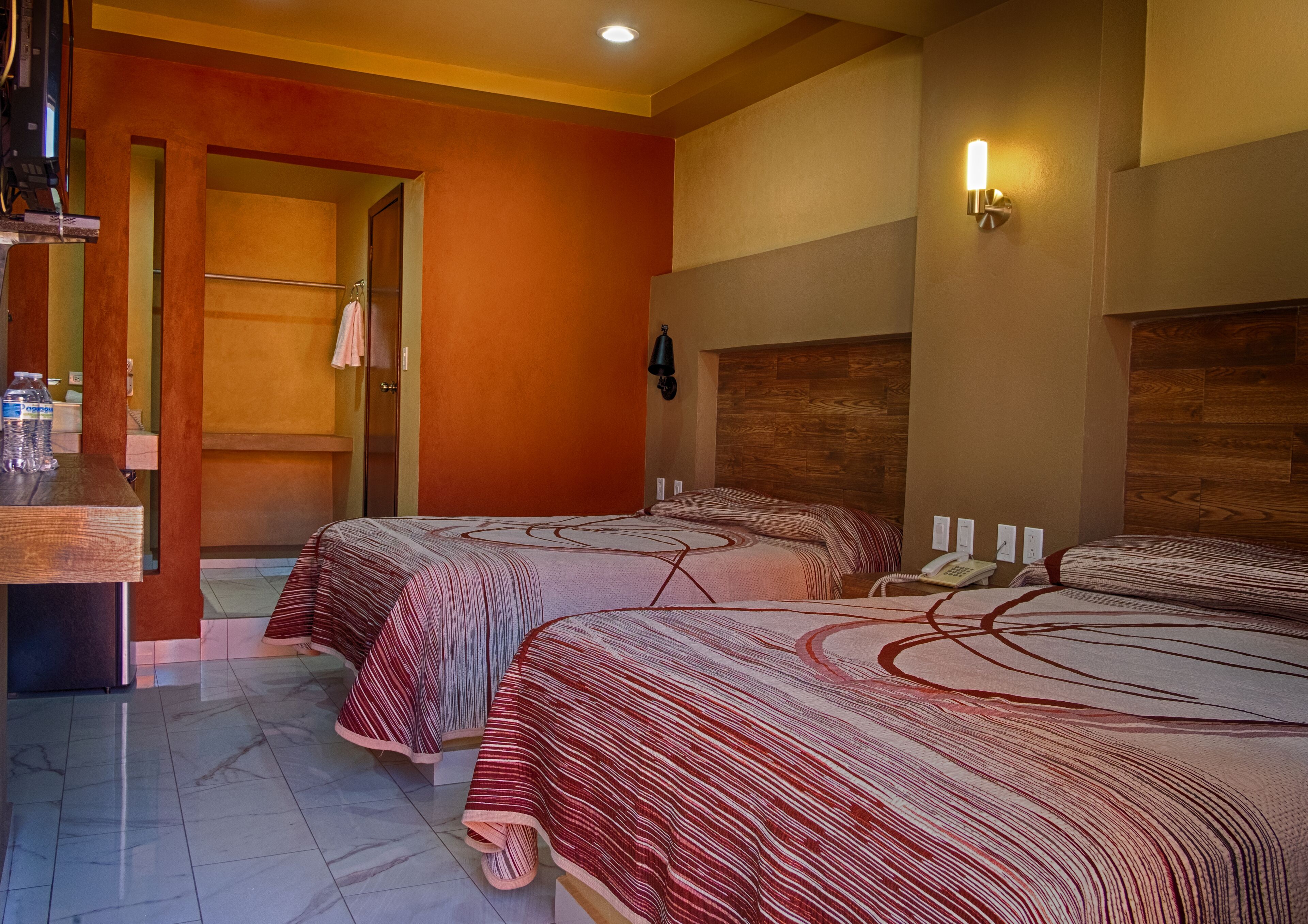 Een hotelkamer met twee bedden, een houten hoofdbord, een badkamer met douche en een tafeltje met een fles water.