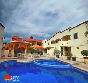 A hotel courtyard with a swimming pool, outdoor seating, and potted plants.