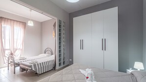 Een slaapkamer met een groot bed, een kleiner bed, een kledingkast en een nachtkastje met een lamp.