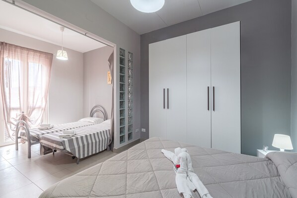 A bedroom with a large bed, a smaller bed, a wardrobe, and a nightstand with a lamp.