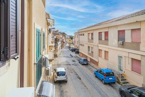 A narrow street with parked cars and buildings on either side.