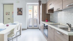 Een moderne keuken met een betegelde spatwand, een eethoek met een witte tafel en stoelen, en een schuifdeur die leidt naar een buitenruimte.