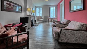 Una sala de estar con piso de madera, una pared de acento roja, un sofá, una silla, una mesa, una lámpara y un televisor.
