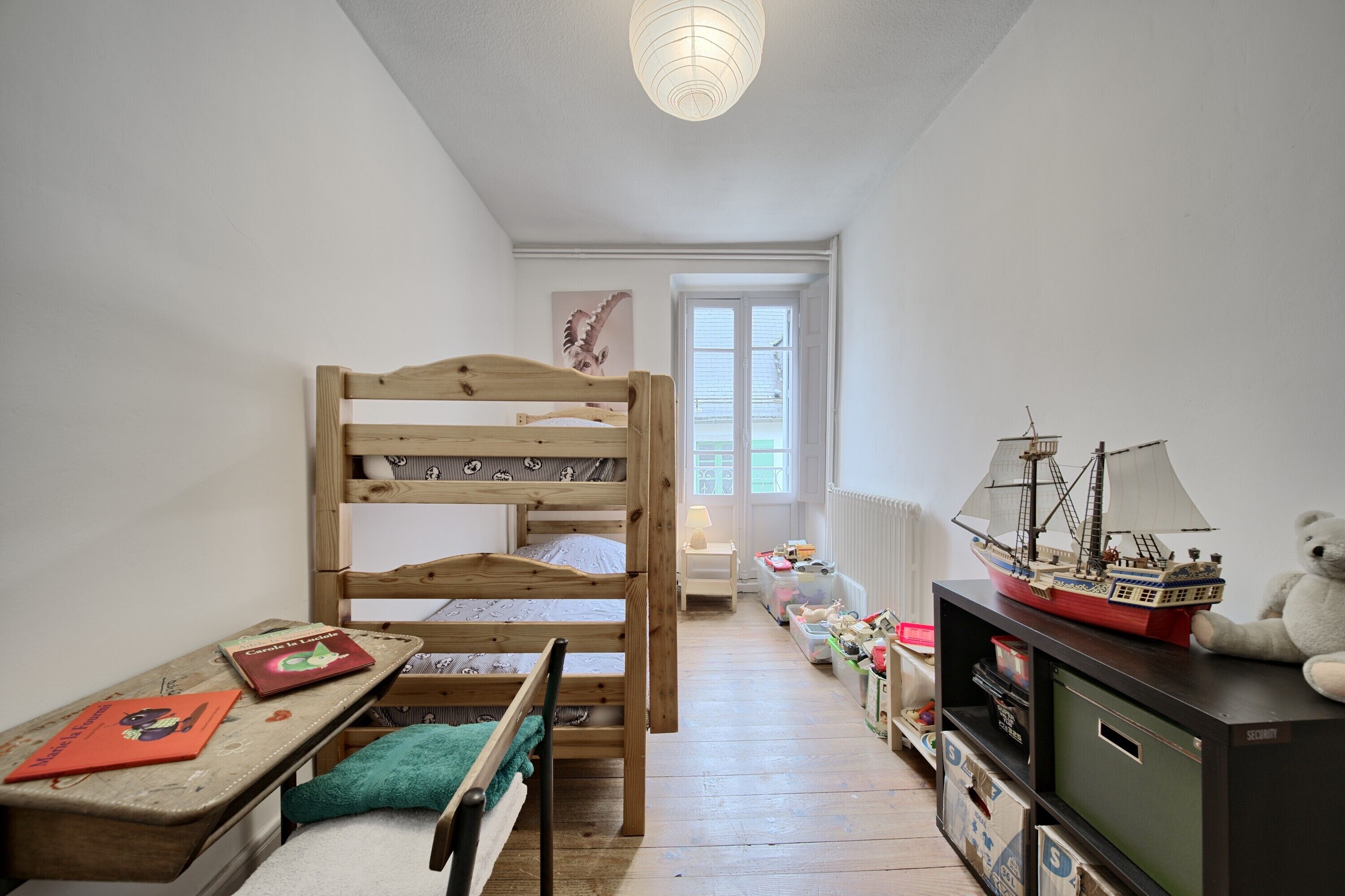 Une chambre d’enfant avec des lits superposés, un bureau, une bibliothèque et une fenêtre.