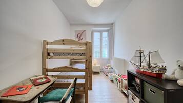 Une chambre d’enfant avec des lits superposés, un bureau, une bibliothèque et une fenêtre.