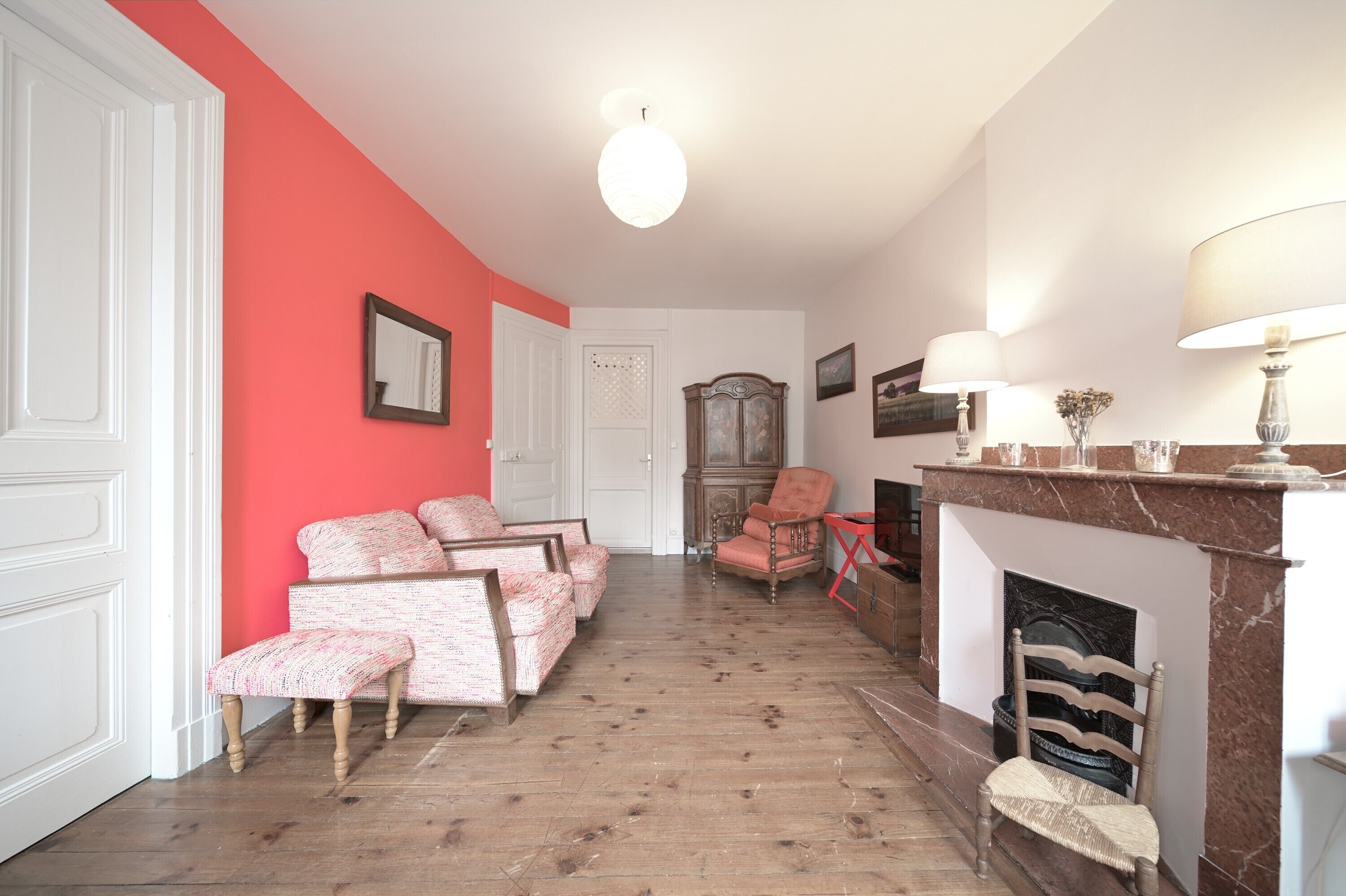 A living room with a red wall, a fireplace, a sofa set, and a wooden floor.
