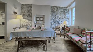 Un comedor con una mesa dispuesta para dos personas, una pared de piedra y un sofá con cojines de colores.