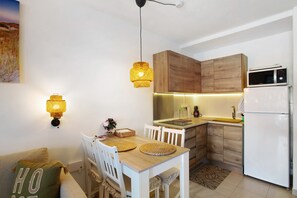 A modern kitchen with wooden cabinets, a white refrigerator, and a dining table with chairs. - Holiday Apartment 'Views Of Sunsets' with Sea View, Shared Pool and Wi-Fi (Taurito)