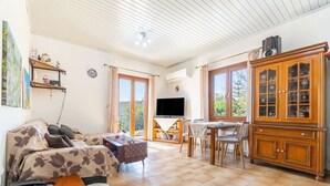 Een woonkamer met een bank, televisie, houten kast en een eethoek met stoelen en een tafel.