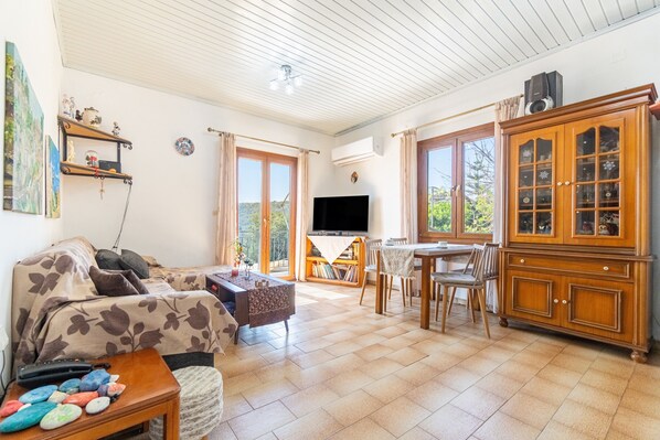A living room with a sofa, TV, wooden cabinet, and a dining area with chairs and a table.