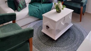 A modern living room with a white sofa, green cushions, a white coffee table, and a green accent wall. - Você Ficará Hospedado a Menos de 5min a pé da Praia de Pitangueiras (Centro Guarujá)