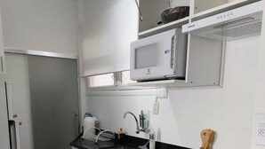 A compact kitchen with white cabinets, a microwave, a stove, and a sink. - Você Ficará Hospedado a Menos de 5min a pé da Praia de Pitangueiras (Centro Guarujá)