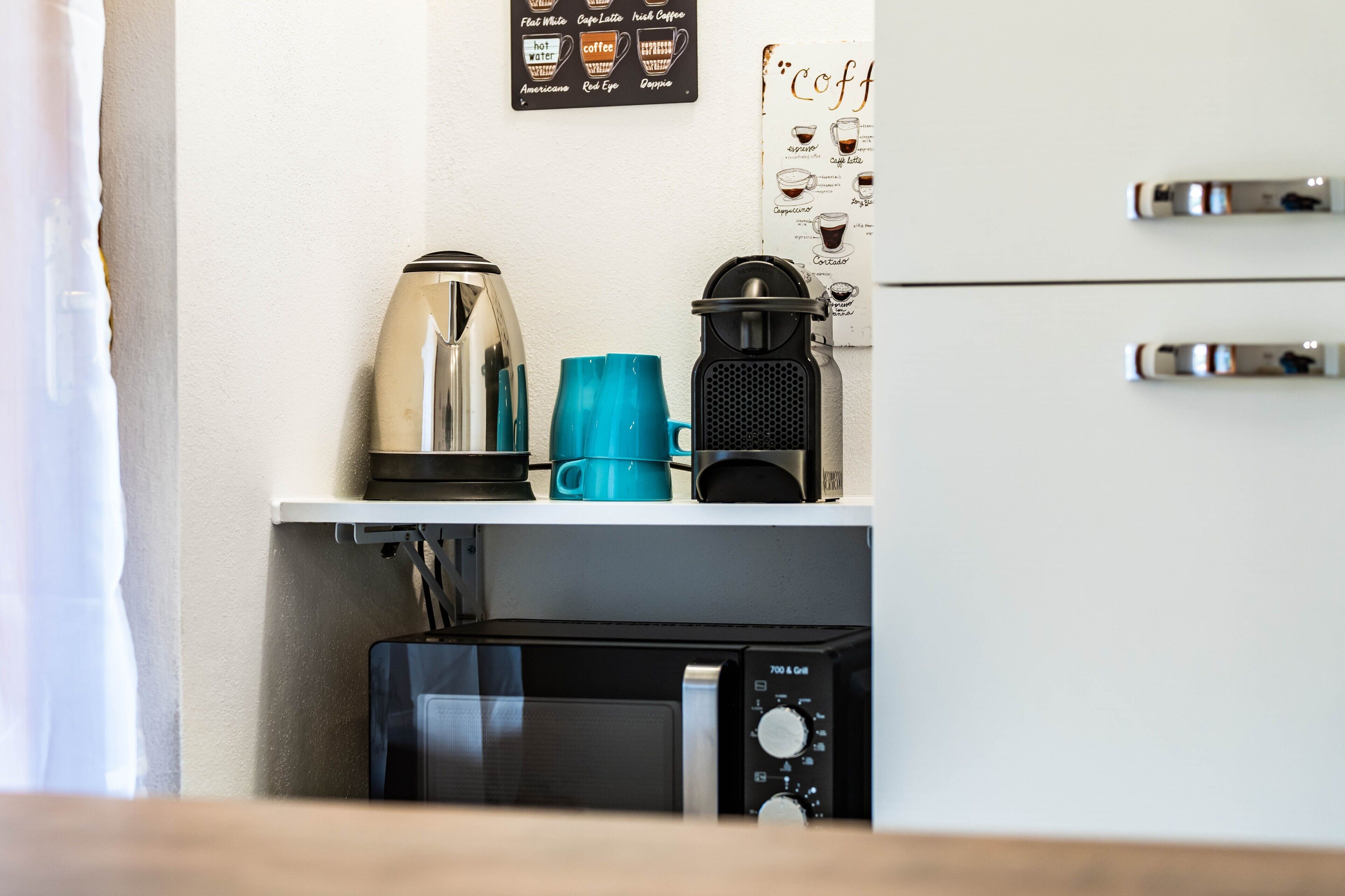 Una kitchenette con cafetera, hervidor, microondas y una taza de café.