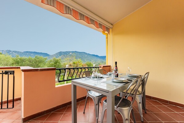 A balcony with a table set for dining, a view of mountains, and a tiled floor.