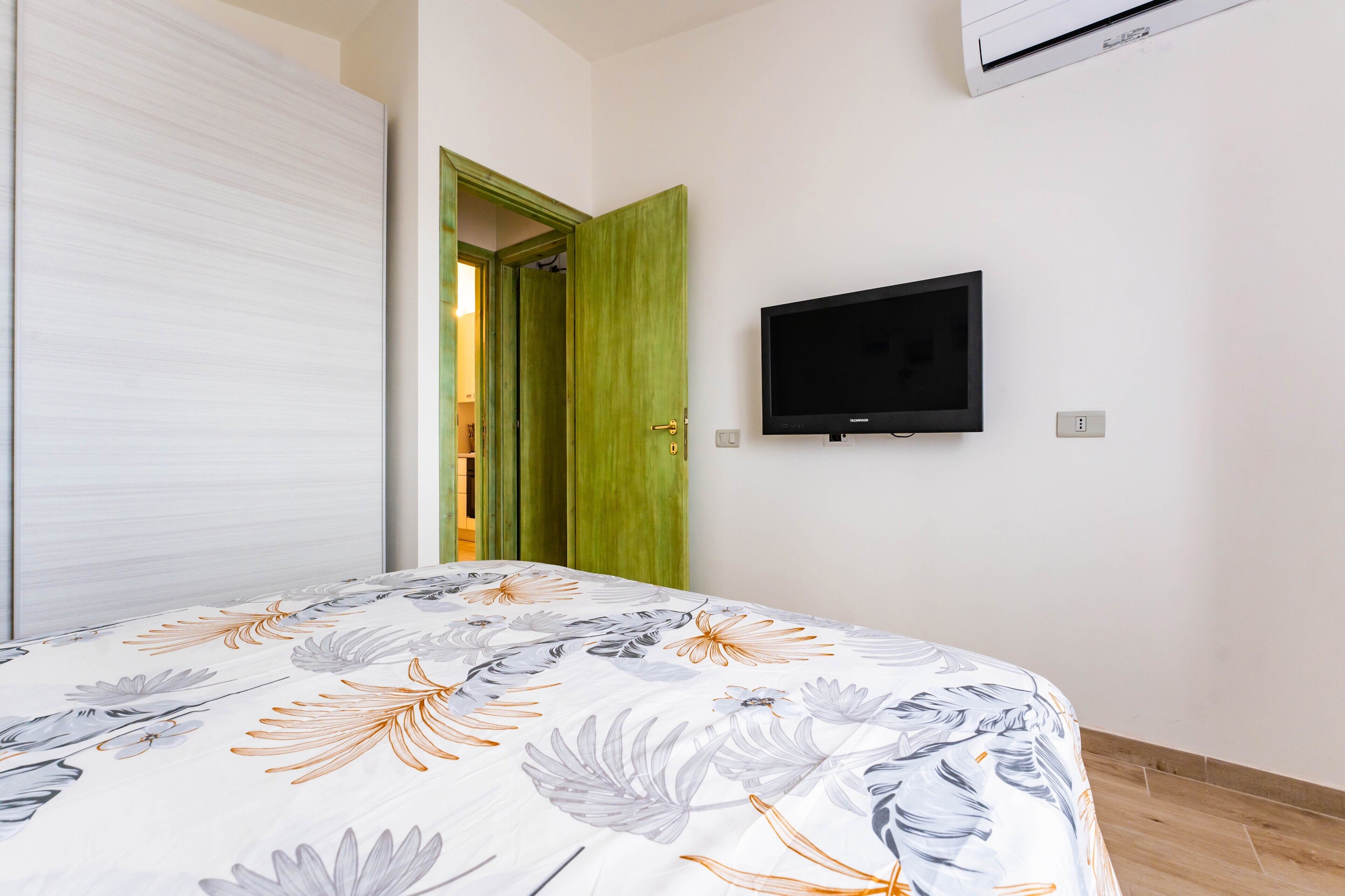 Ein Schlafzimmer mit Bett, Fernseher, Kleiderschrank und einer grünen Tür.