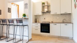 A modern kitchen with white cabinets, a gas stove, and a dishwasher. There are bar stools and a potted plant. - Apartment 'Dimora Frau' with Shared Pool, Wi-Fi and Air Conditioning (Villasimius)