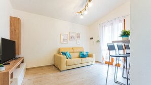 A living room with a sofa, a TV, and a dining area with chairs. - Apartment 'Dimora Frau' with Shared Pool, Wi-Fi and Air Conditioning (Villasimius)