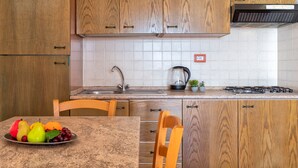 A kitchen with wooden cabinets, a stainless steel sink, a gas stove, and a fruit bowl on the table. - Apartment 'Rosa's' with Sea View and Private Terrace (Isola Rossa)